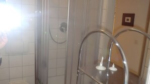 Un bany amb box de dutxa de vidre, vàter blanc i un lavabo amb aixeta cromada.