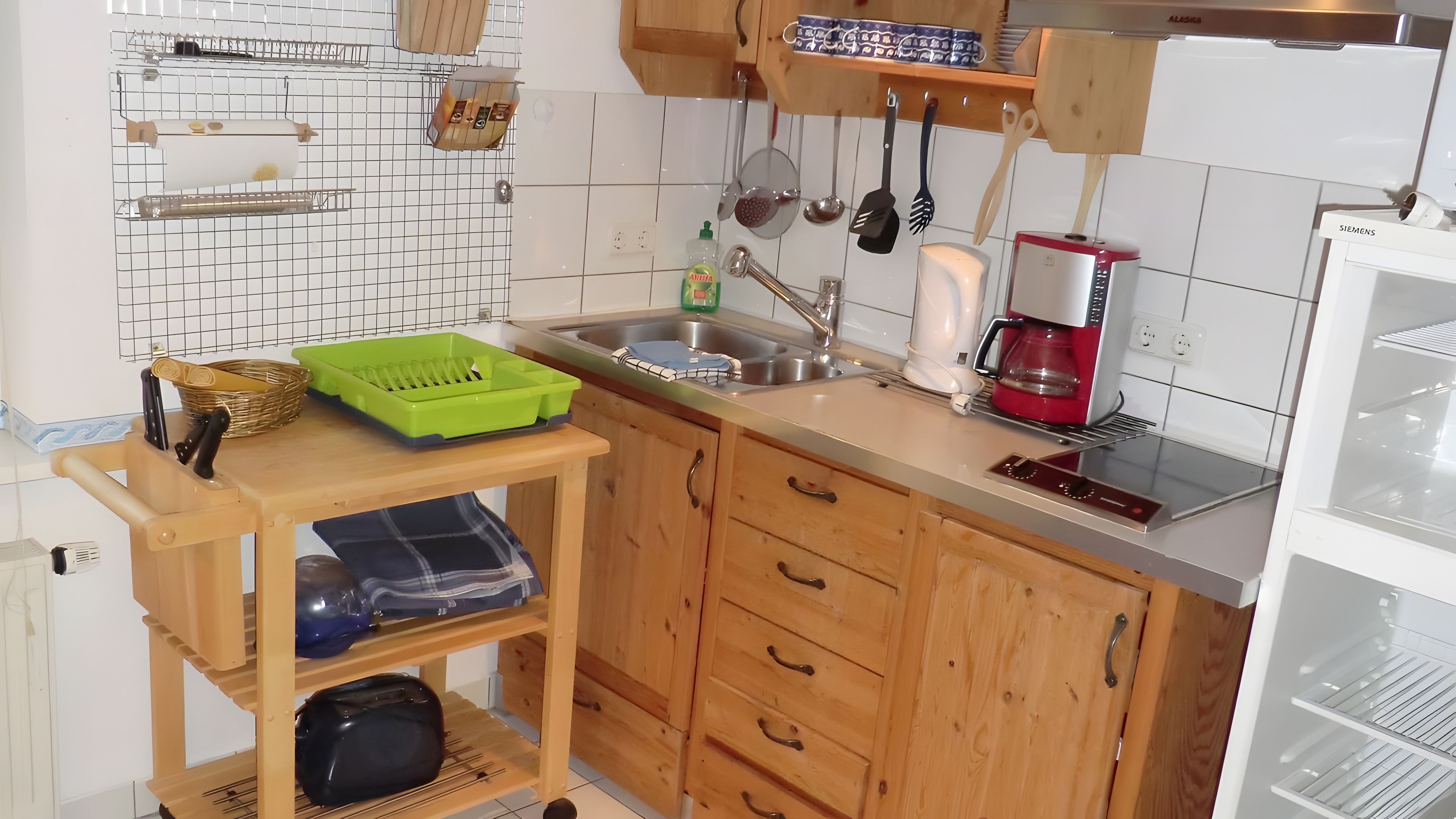 Eine Küche mit Holzschränken, einem Spülbecken, einer Kaffeemaschine und einem grünen Plastikbehälter auf einem Holzboden.