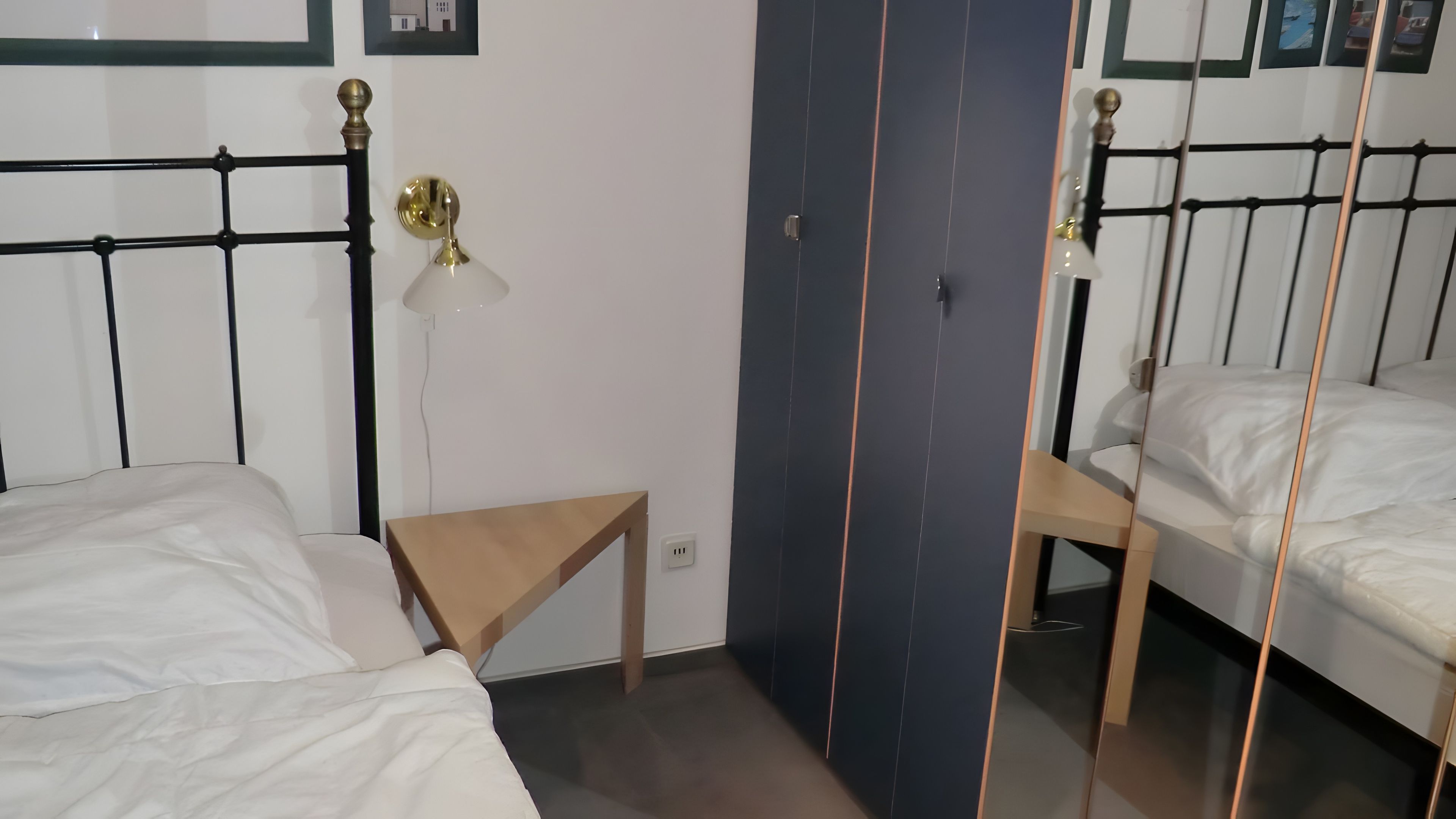 Ein Zimmer mit zwei Betten, einem kleinen Tisch, einer Wandlampe und einer Tür mit Spiegel.