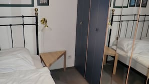 Ein Zimmer mit zwei Betten, einem kleinen Tisch, einer Wandlampe und einer Tür mit Spiegel.