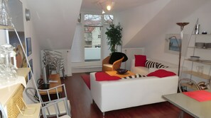 Ein modernes Wohnzimmer mit einem weißen Sofa, roten Kissen, einem Esstisch und einer Pflanze.