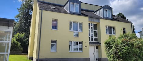 A multi-story residential building with a flat roof, multiple windows, and a visible entrance.