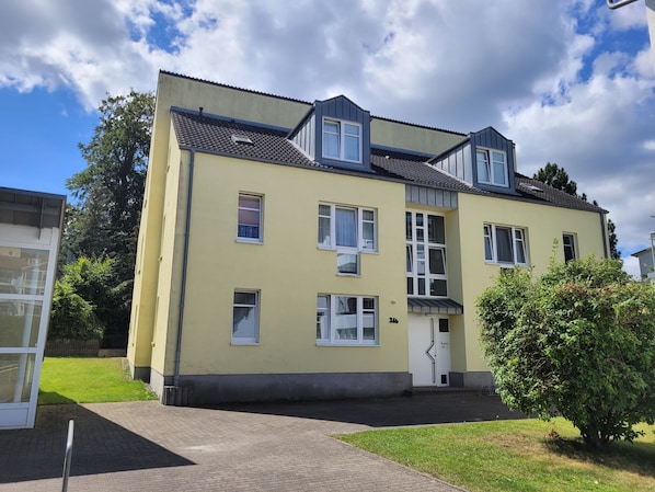 Ein zweistöckiges Gebäude mit flachem Dach, zahlreichen Fenstern und einer kleinen Veranda.