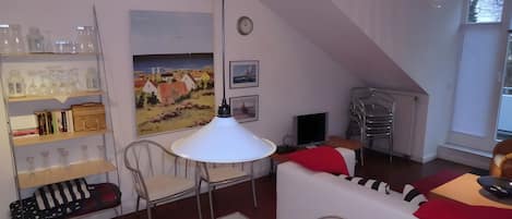 Uma sala de estar aconchegante com um sofá branco, uma mesa de jantar e uma estante de livros.