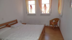 Ein Schlafzimmer mit einem Einzelbett, einem Sessel und zwei fensterbepflanzten Fenstern.