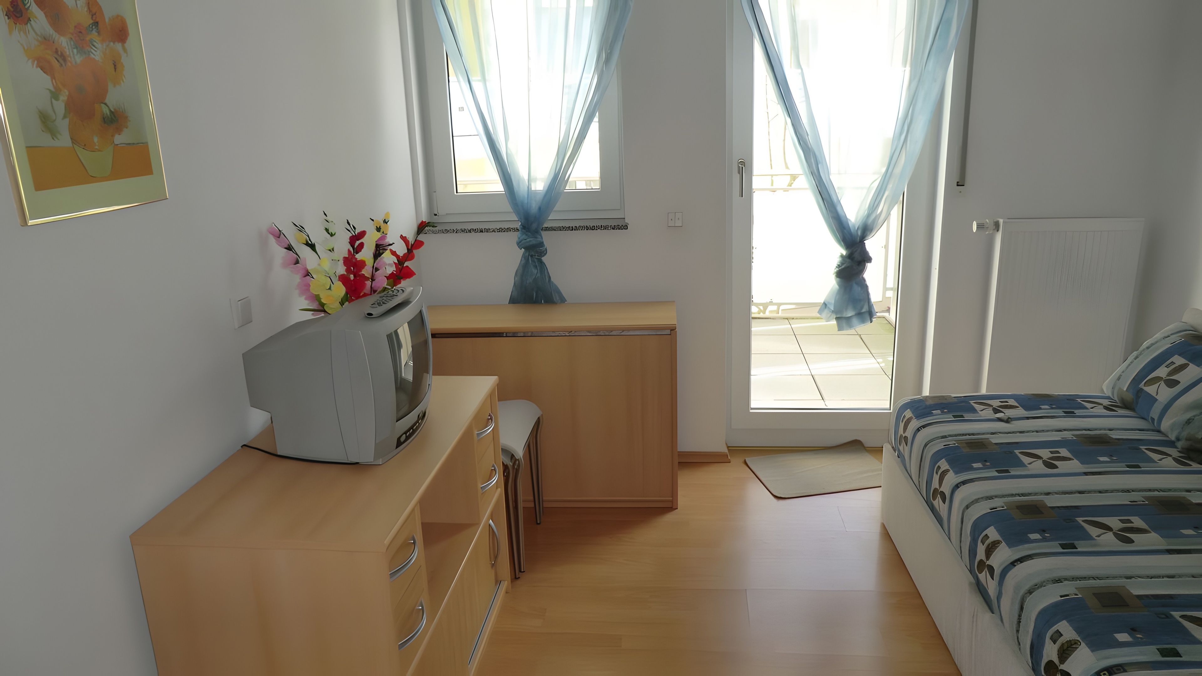 Ein Zimmer mit einem Bett, einem Schreibtisch mit Fernseher, einem Fenster mit Vorhängen und einer Heizung.