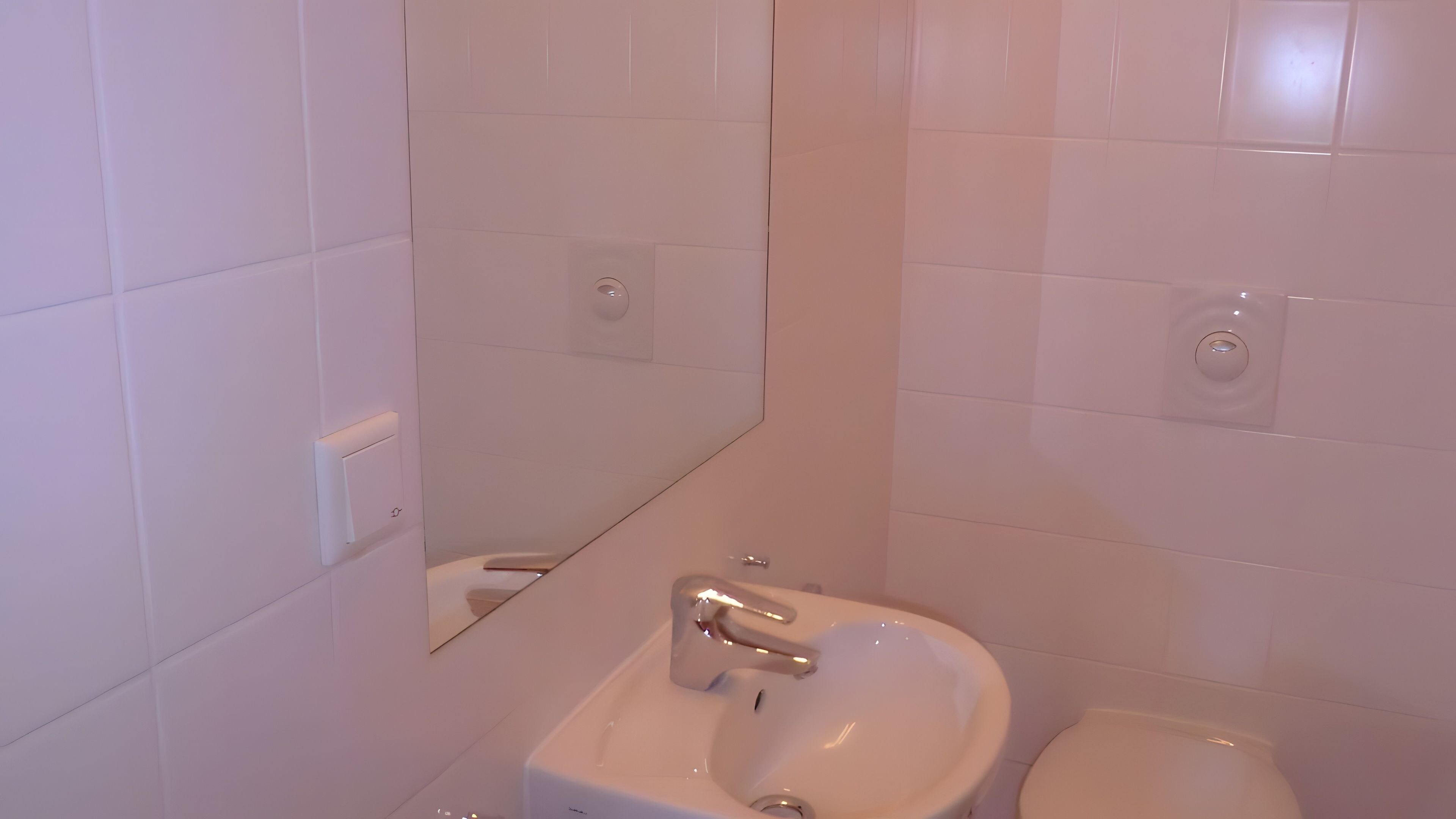Ein Badezimmer mit weißen Fliesen, einem Waschbecken, einem Spiegel und einer Toilette.
