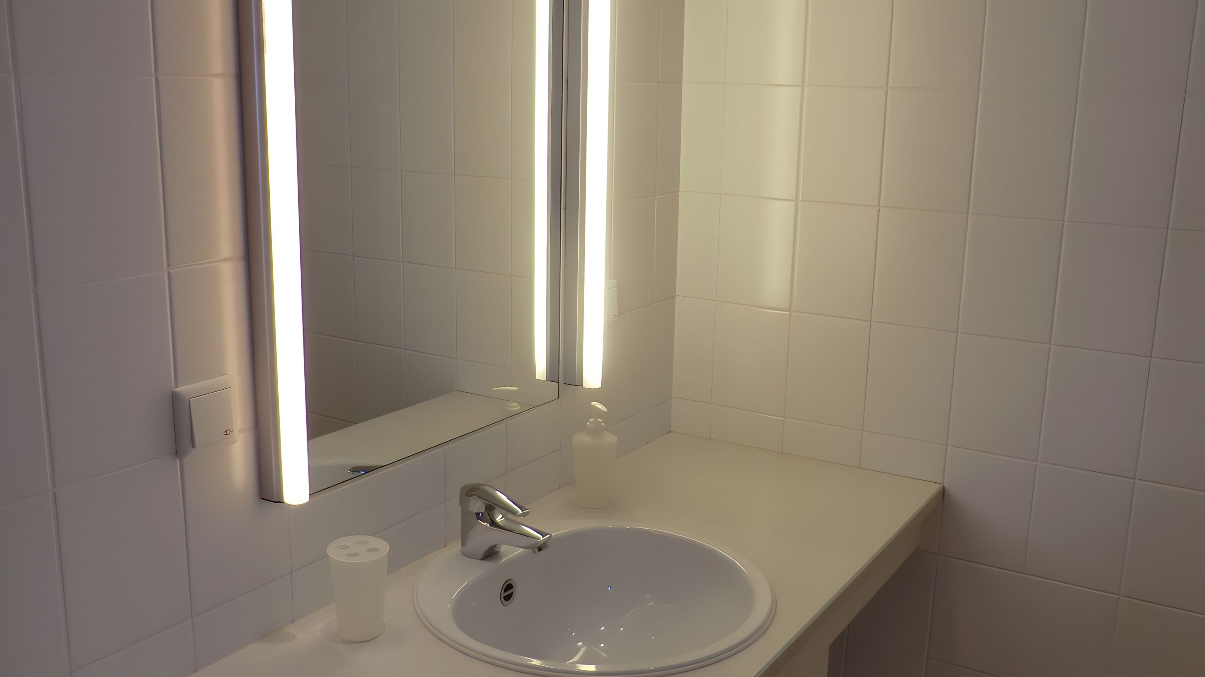 Ein Badezimmer mit einem weißen Waschbecken, einem Spiegel und einer Leuchte darüber.