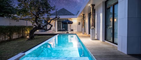 Un área de piscina moderna al aire libre con vista despejada del cielo nocturno, una terraza de madera y una silla de descanso.