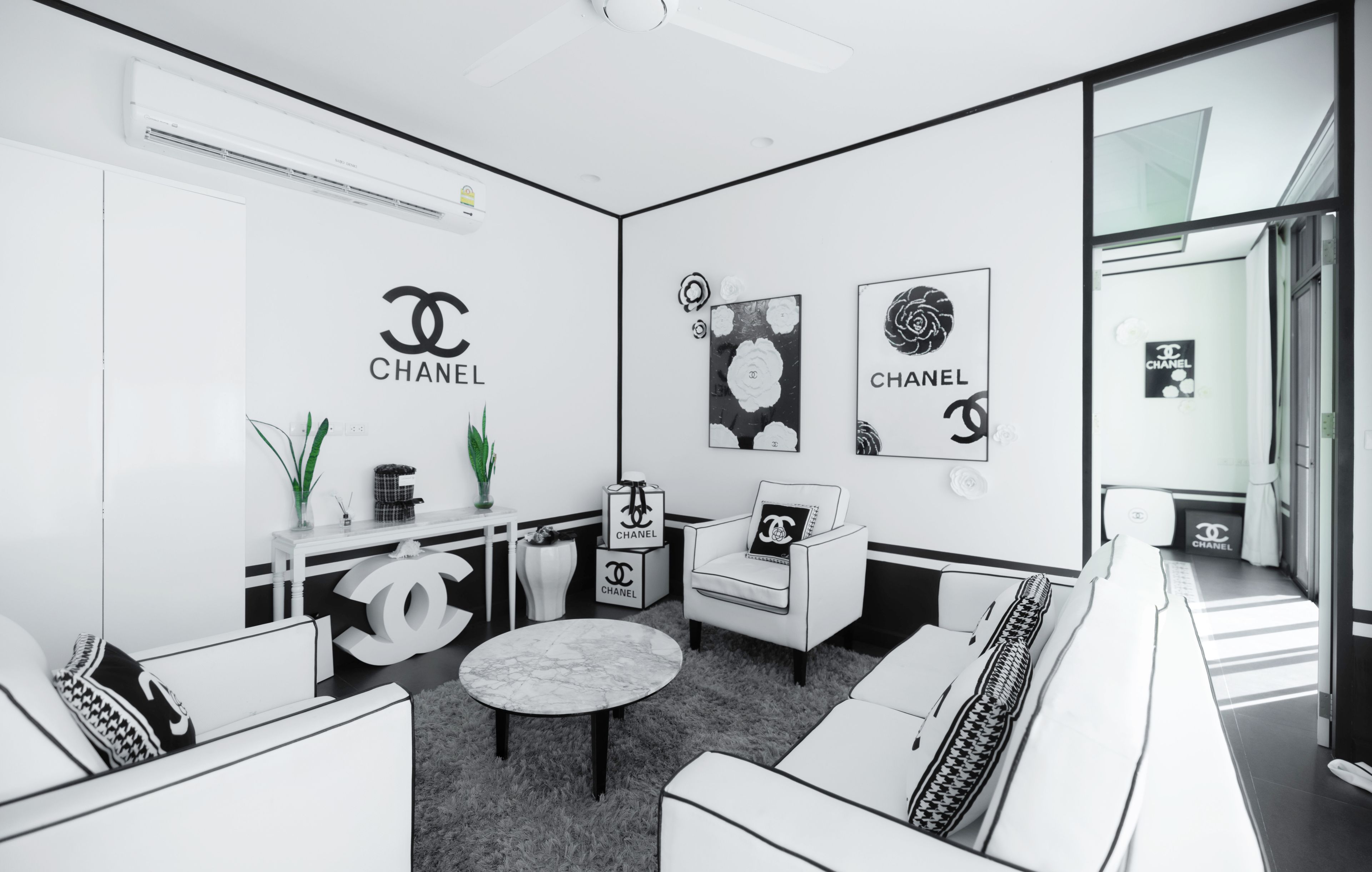 A modern, monochrome interior with a minimalist design, featuring a sofa set, a round table, and a chair with a Chanel logo.