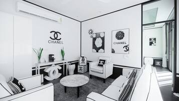 A modern, monochrome interior with a minimalist design, featuring a sofa set, a round table, and a chair with a Chanel logo.