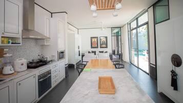 A modern kitchen with white cabinets, a wooden dining table, and a view through large windows.