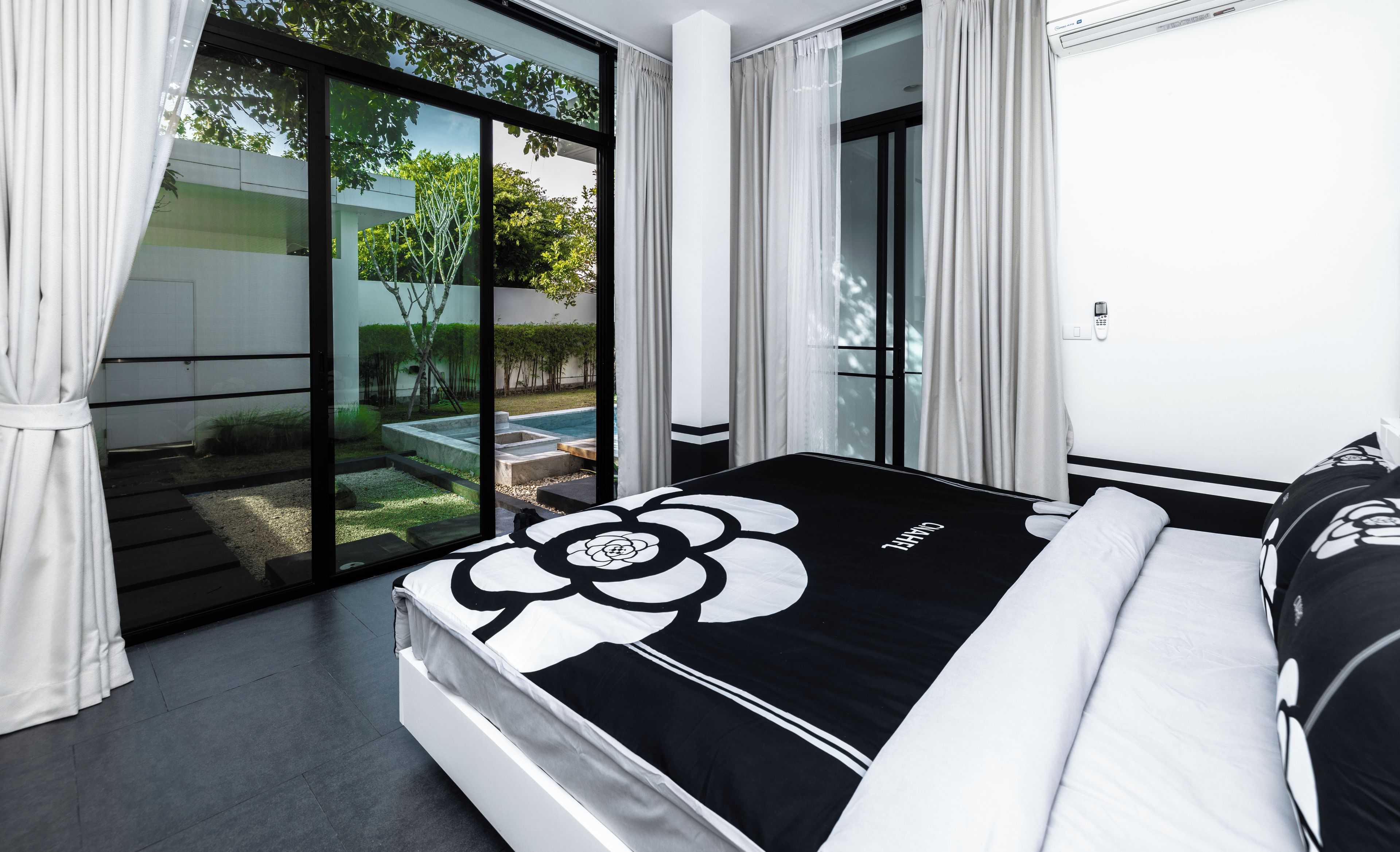 A modern bedroom with a large bed, a view of a garden, and a sliding glass door.
