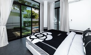 A modern bedroom with a large bed, a view of a garden, and a sliding glass door. - Chalong 3bed-room seaside pool villa  (Tambon Chalong)