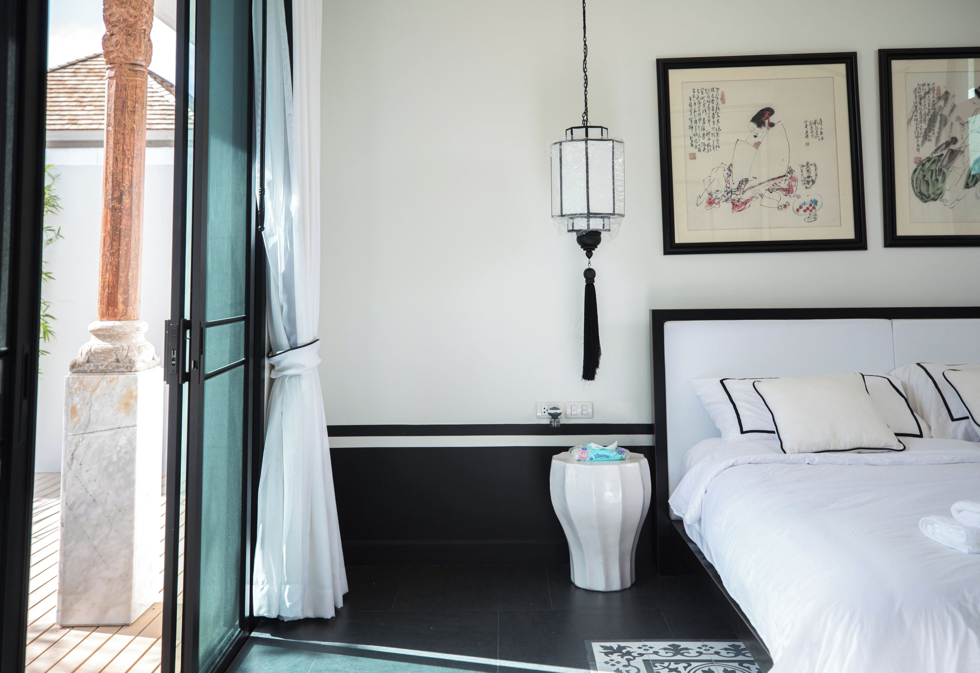 A hotel room with a bed, a nightstand, a hanging light fixture, and artwork on the wall.