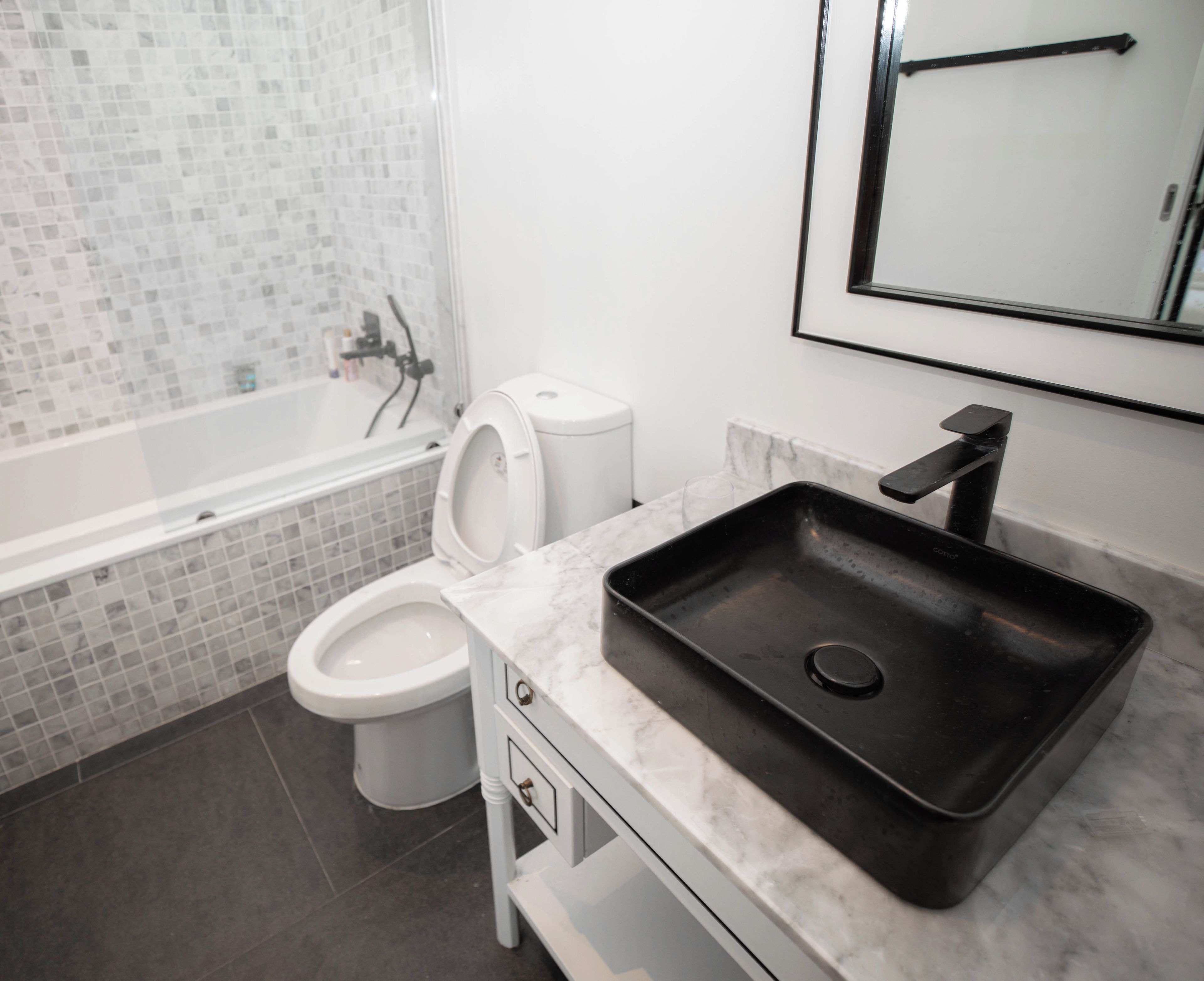 Un baño moderno con bañera, inodoro y un lavabo negro sobre encimera de mármol.