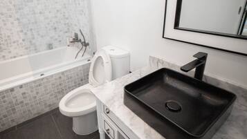 Un baño moderno con bañera, inodoro y un lavabo negro sobre encimera de mármol.