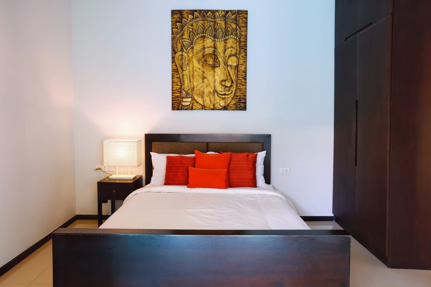 A bedroom with a bed, pillows, a nightstand, a lamp, and a wall-mounted artwork.