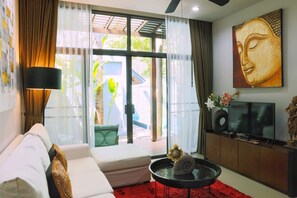 A modern living room with a sofa, a coffee table, a TV, and a Buddha painting. - Tranquil Rawai villa with pool and tropical garden (Tambon Rawai)