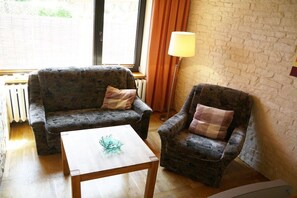A room with a sofa, armchair, and a small table with a glass object. - Holiday apartment with 1 bedroom (Ostseebad Prerow)