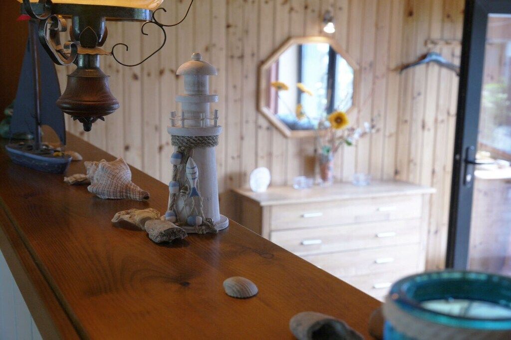 Una encimera de madera con objetos decorativos, incluyendo una maqueta de faro, conchas marinas y un tazón azul.