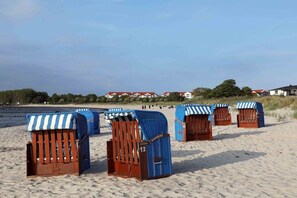 Des cabanes de plage avec des auvents rayés, sur une plage de sable, avec des maisons en arrière-plan.