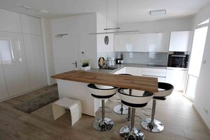 A modern kitchen with white cabinetry, a wooden island, and two bar stools. - Holiday apartment in Glowe with swimming pool (Glowe)