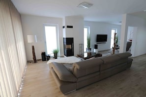 A modern living room with a large sofa, a flat-screen TV, and a fireplace. - Holiday apartment in Glowe with swimming pool (Glowe)