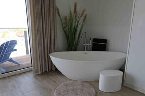 Une salle de bain moderne avec une baignoire sur pieds, un petit tabouret et une plante en pot.
