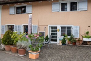 Ein Gebäude mit vielen Fenstern, einige mit Fensterläden, und verschiedenen Blumentöpfen im Vorbereich.