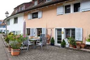 Ein Gebäude mit Kopfsteinpflasterstraße, Außenbereich mit Stühlen und Tisch sowie Blumentöpfen.