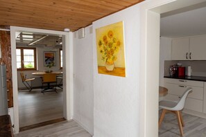 Ein Zimmer mit Esstisch und Stühlen, einer Küchenzeile mit Schränken und einem Gemälde von Sonnenblumen an der Wand.