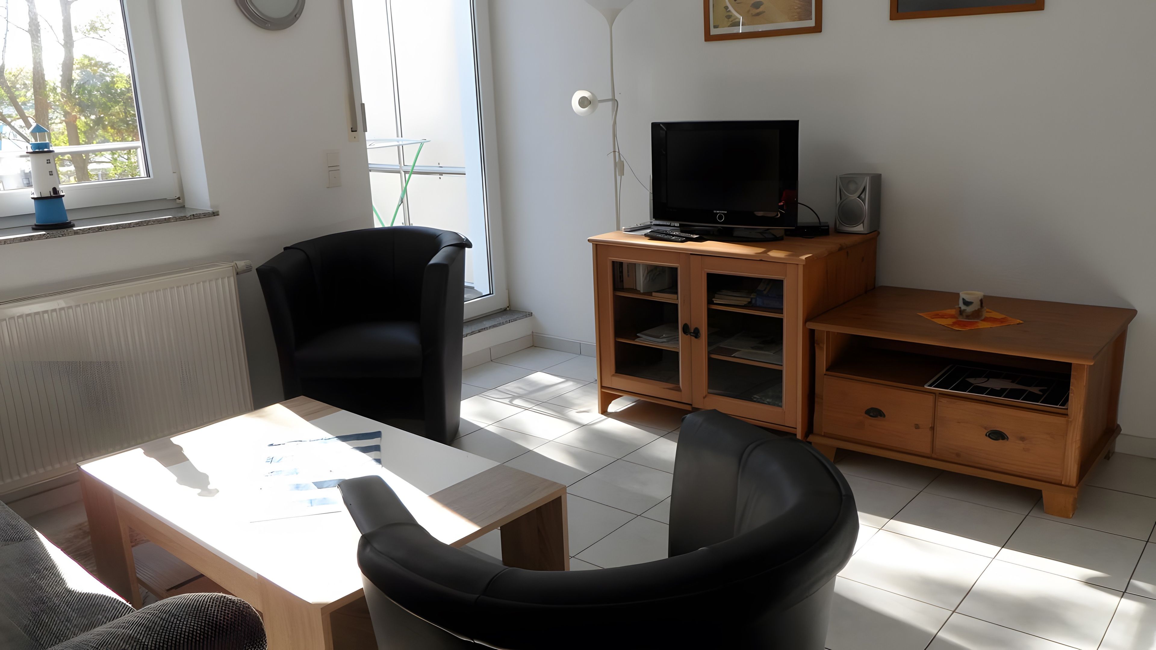 Ett rum med en svart stol, ett träbord, en tv på ett träställ och ett skåp med glasdörrar.