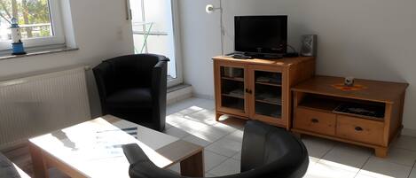 Ett rum med en svart stol, ett träbord, en tv på ett träställ och ett skåp med glasdörrar.