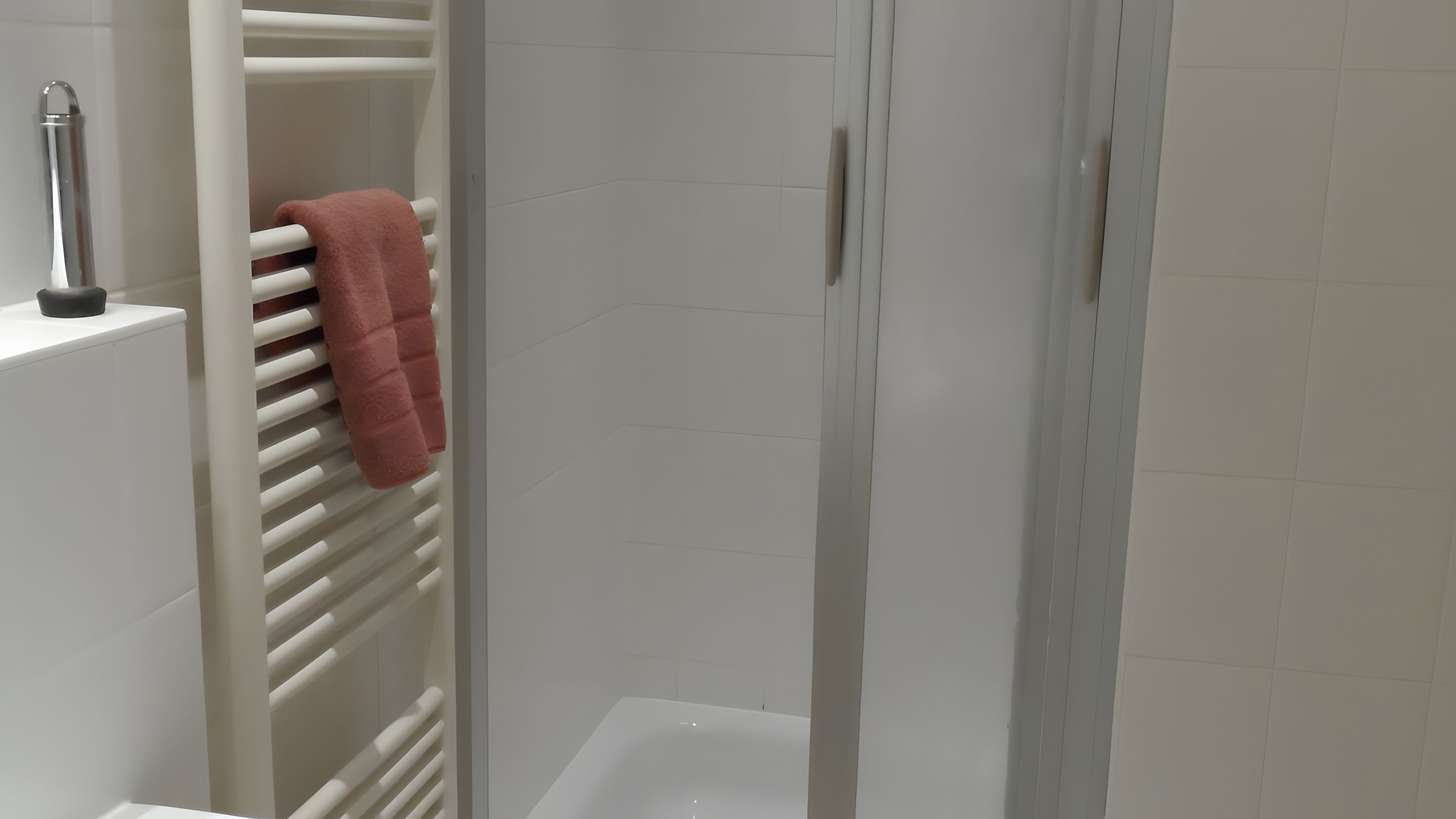 Ein Badezimmer mit einer weißen Badewanne, einem Handtuchhalter mit einem rosafarbenen Handtuch und einer weißen Fliesenwand.