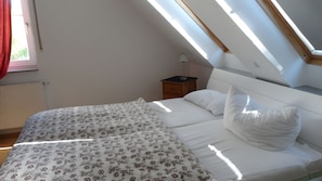 Ein Schlafzimmer mit Dachfenster, einem Bett mit weißer Bettwäsche und einem Nachttisch mit Lampe.