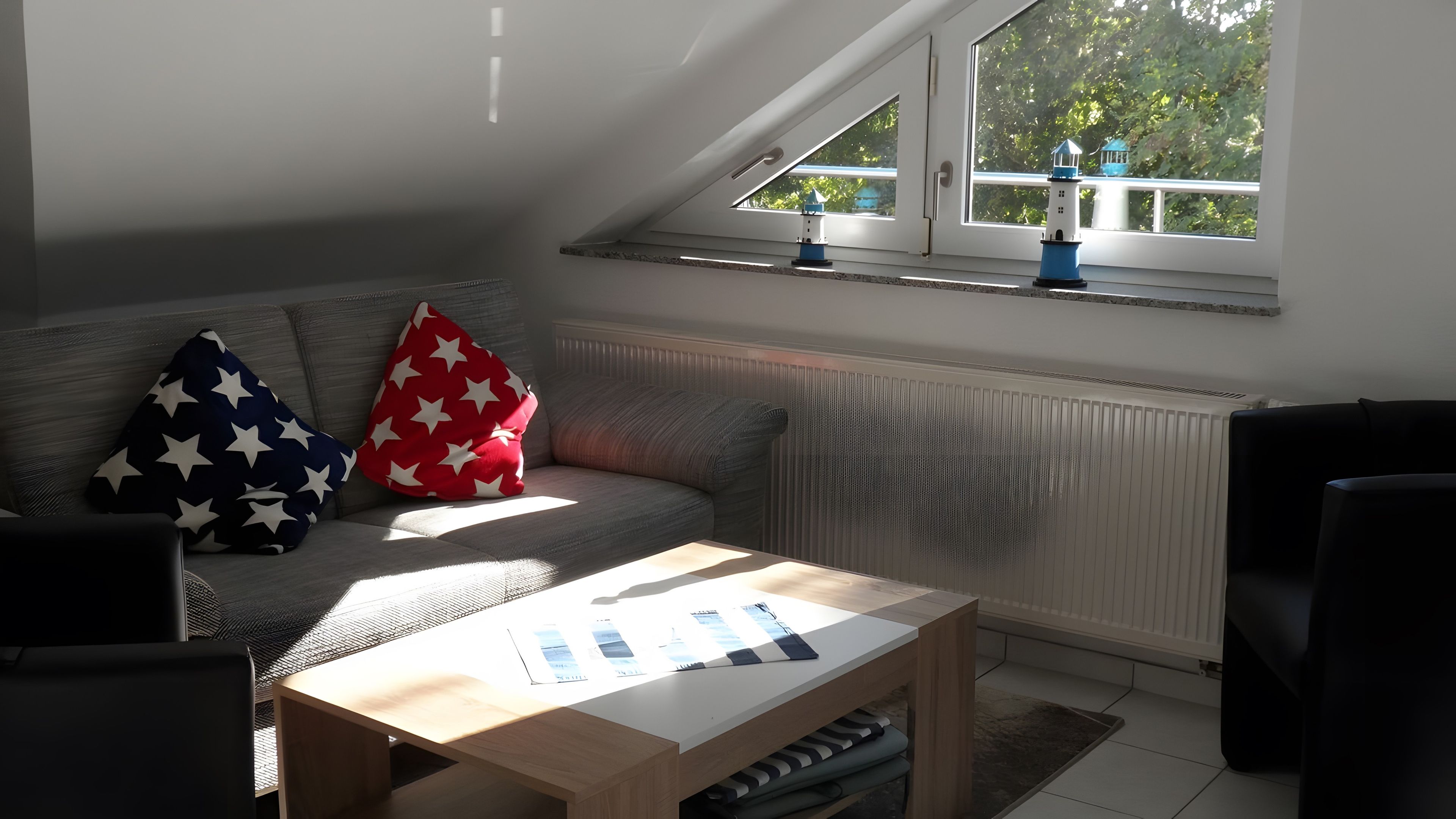 Ein modernes Wohnzimmer mit schrägem Dach, einer Couch mit sternenmusterten Kissen, einem Couchtisch und Blick auf Bäume durch ein Fenster.