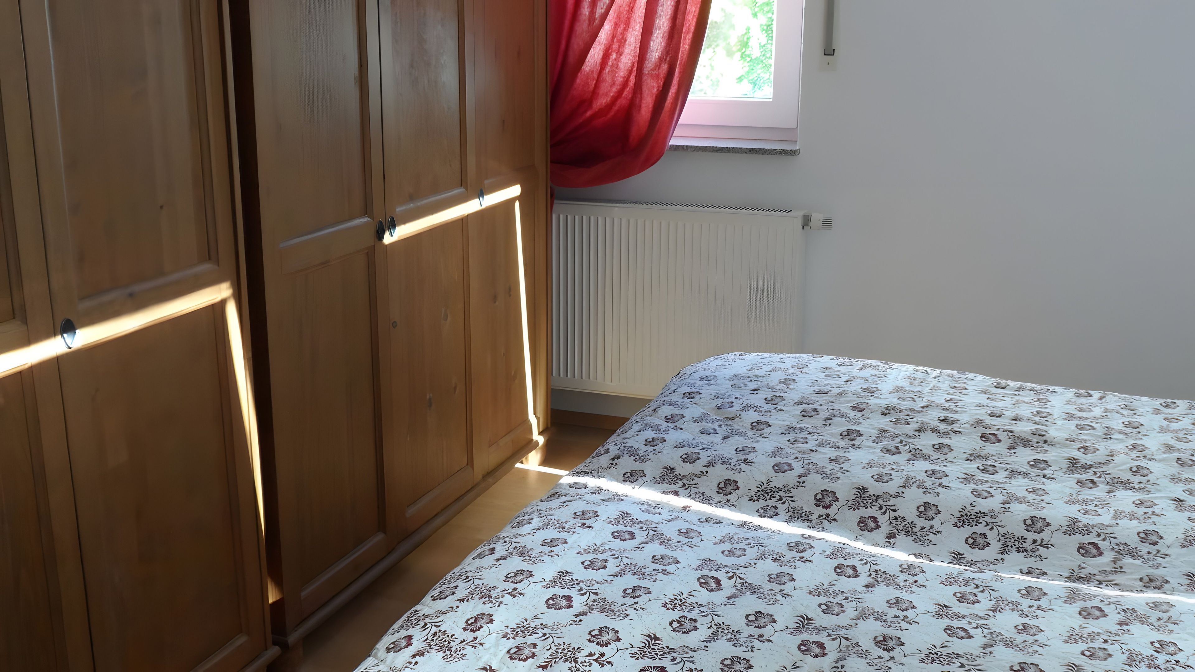 Ein Schlafzimmer mit einem Holzschrank, einem Heizkörper und einem Bett mit floralem Überwurf.