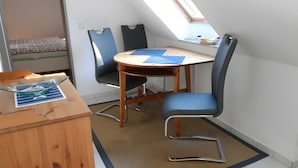 Habitació petita i moderna amb escriptori de fusta, dues cadires, taula petita i finestra al sostre amb inclinació.