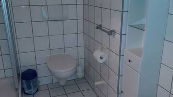 Ein kleines Badezimmer mit Toilette, Mülleimer und Toilettenpapierhalter.