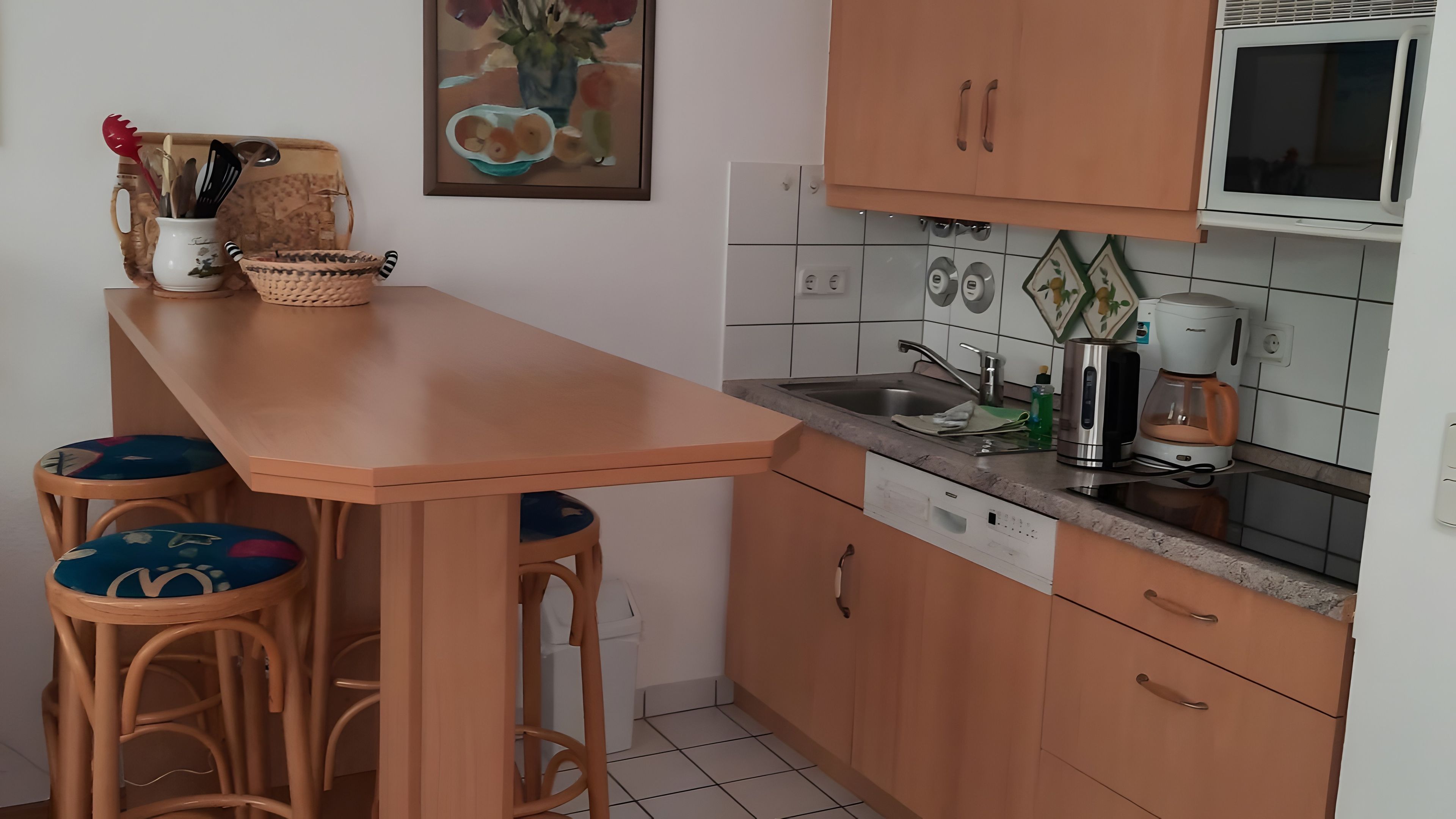 Eine Küche mit einer Holzausziehtheke, zwei Barhocker, einer Kaffeemaschine und einer Mikrowelle.