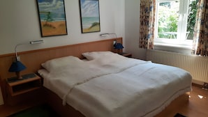 Habitació d'hotel amb un llit, dues làmpades de nit, una finestra amb cortines i dos quadres murals.