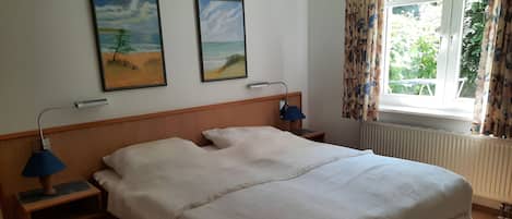 Ein Hotelzimmer mit einem Bett, zwei Nachttischlampen, einem Fenster mit Vorhängen und zwei Bildern an der Wand.