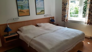 Ein Hotelzimmer mit einem Bett, zwei Nachttischlampen, einem fensterbelaubten Fenster und zwei Wandbildern.