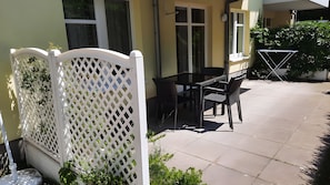 Eine Terrassengruppe im Freien mit Tisch und Stühlen, ein weißes Gitter und ein Blumentopf.