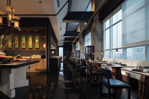 Un restaurante moderno con una barra larga, sillas de madera y vistas a la ciudad a través de amplios ventanales.