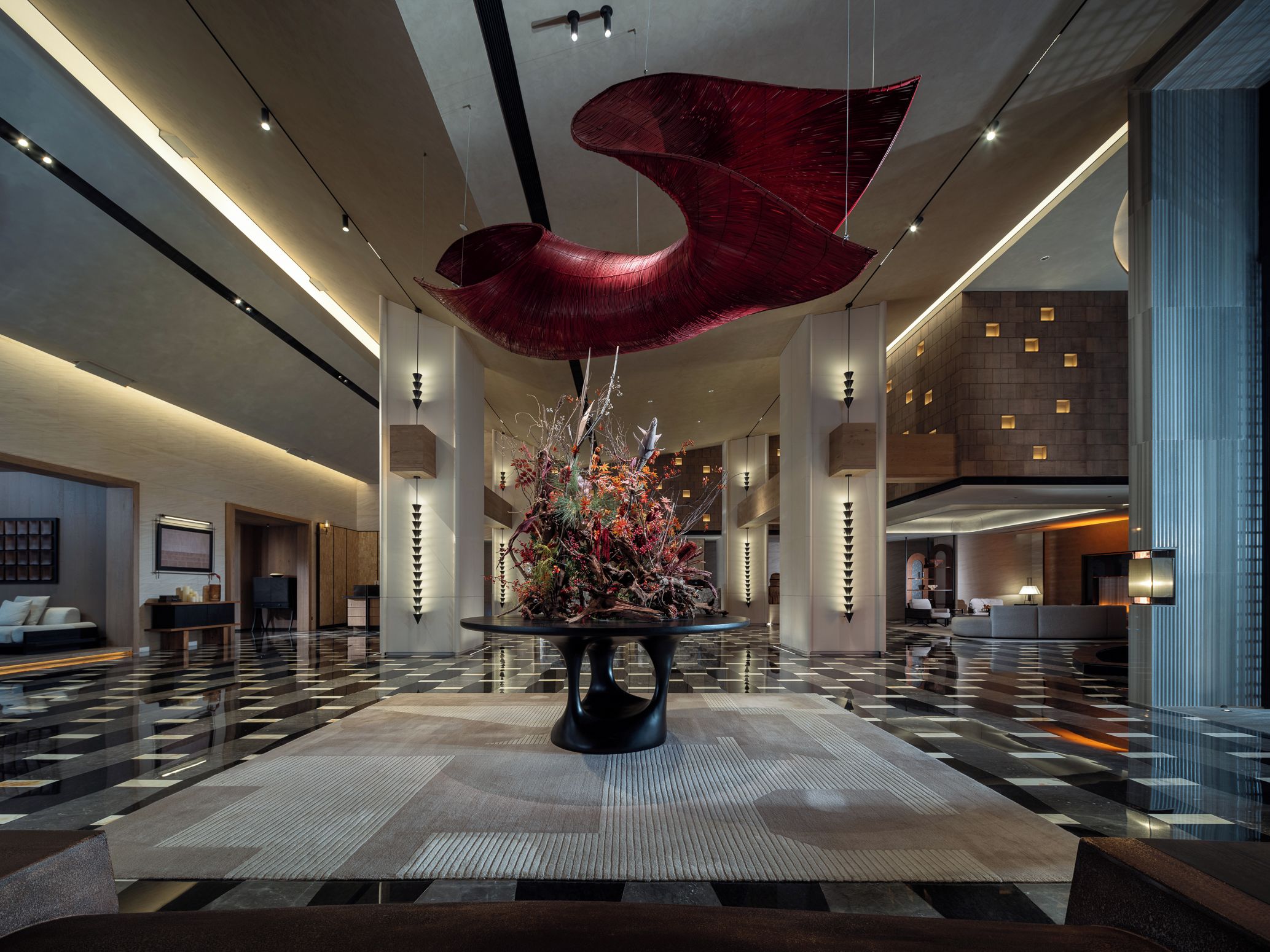 A spacious lobby with a central floral arrangement, high ceilings, and modern lighting fixtures.