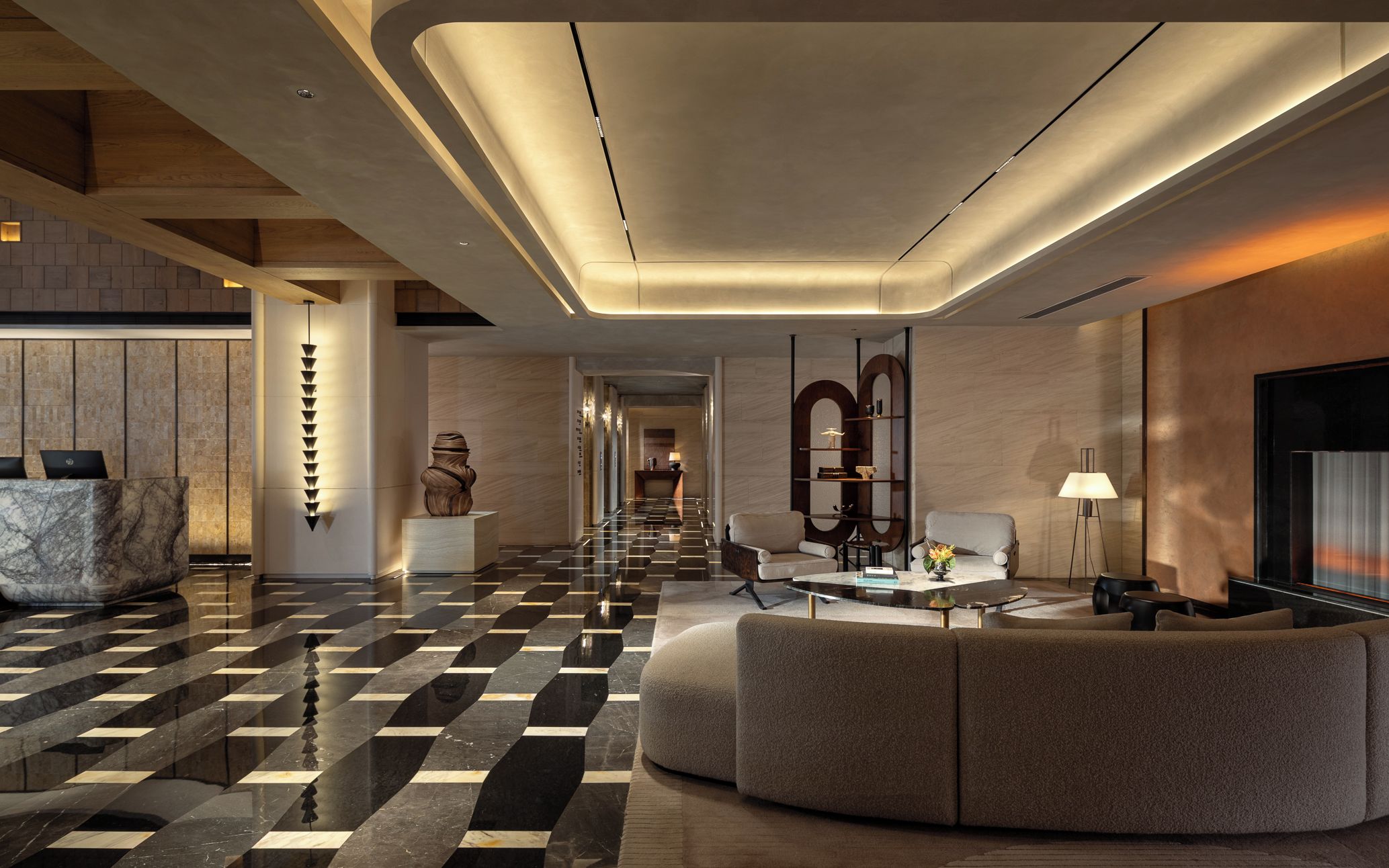 A modern hotel lobby with a checkered floor, a reception desk, seating area, and a large wall-mounted TV.