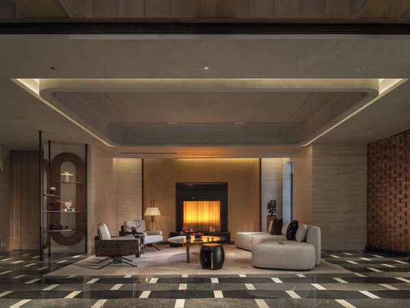 A modern lobby with a sofa, armchairs, a coffee table, and a fireplace.