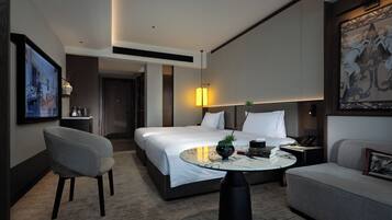 Ein modernes Hotelzimmer mit einem Bett, einem runden Couchtisch, einer Couch, einem Sessel und einem Bild an der Wand.